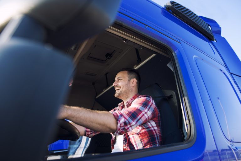 Motorista de caminhão sorrindo dentro da cabine de um caminhão azul, representando transporte de cargas e financiamento de veículos pesados.