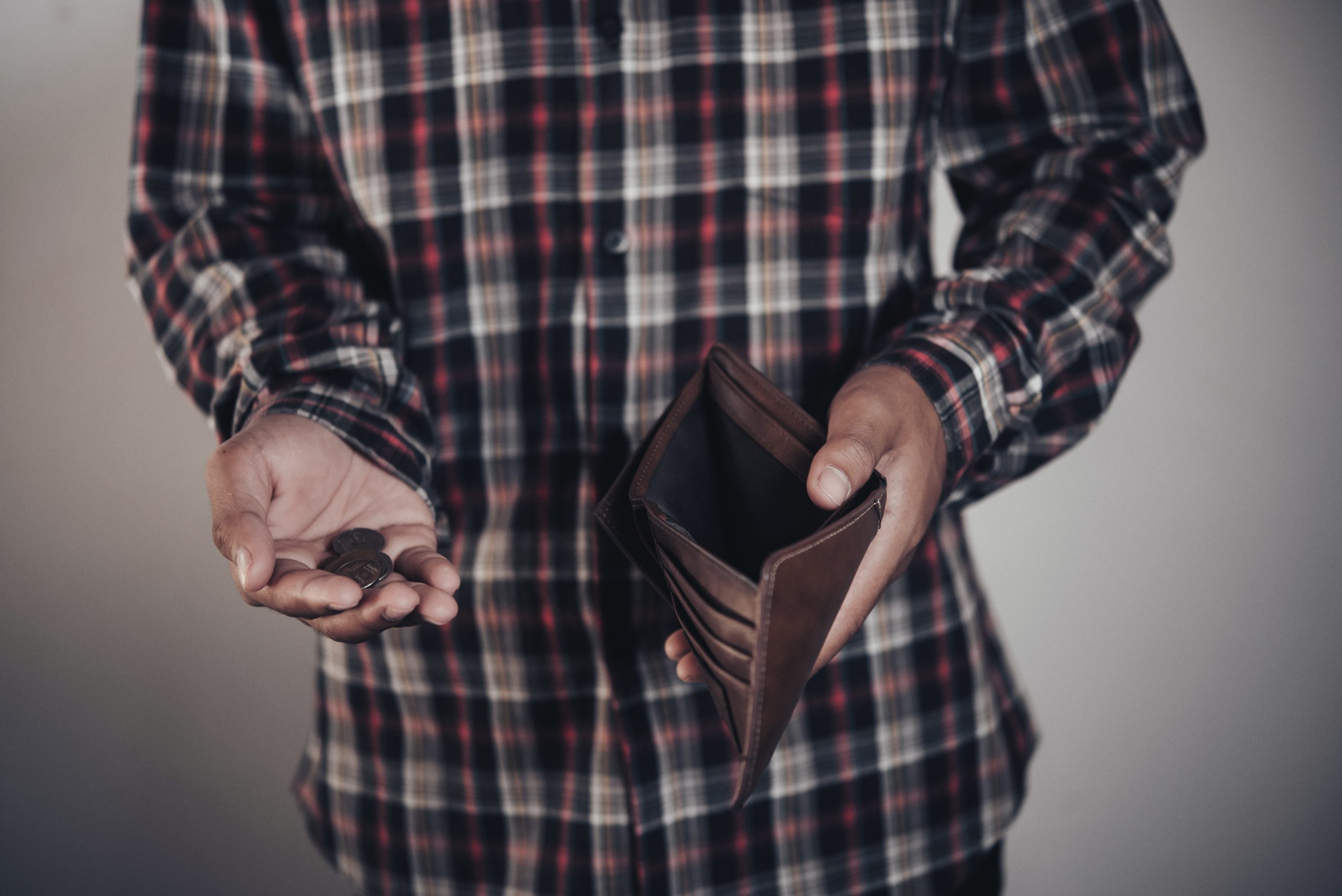 Pessoa segurando carteira aberta com poucas moedas na mão, representando falta de dinheiro e orçamento apertado.