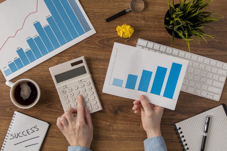 Pessoa analisando gráficos financeiros e calculadora sobre mesa de trabalho, representando planejamento financeiro e definição de metas.