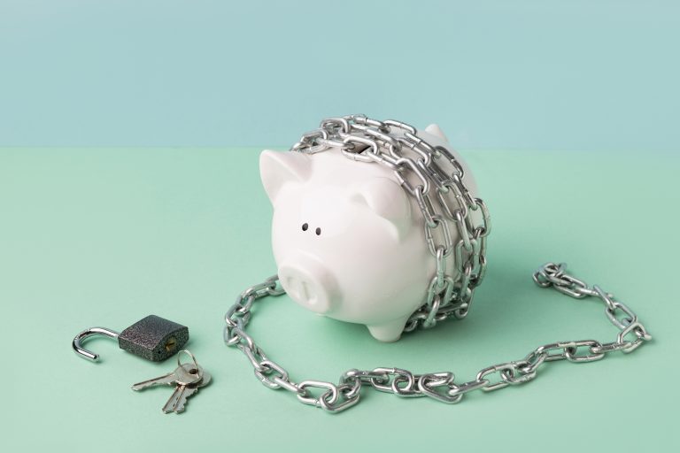 Porquinho de cerâmica preso por cadeado e corrente, simbolizando limitações financeiras e dificuldades de acesso a recursos.